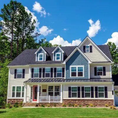 Two-story home exterior with tan and blue-gray siding, stone base, and red front door