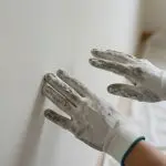 Gloved hands pressing on a fresh white wall to assess paint durability