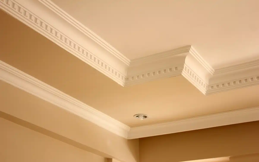 White decorative crown molding along a tan ceiling and wall corner