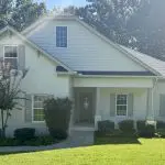 Two-story cream brick home with gray shutters showing UV exposure and paint fading in direct sun