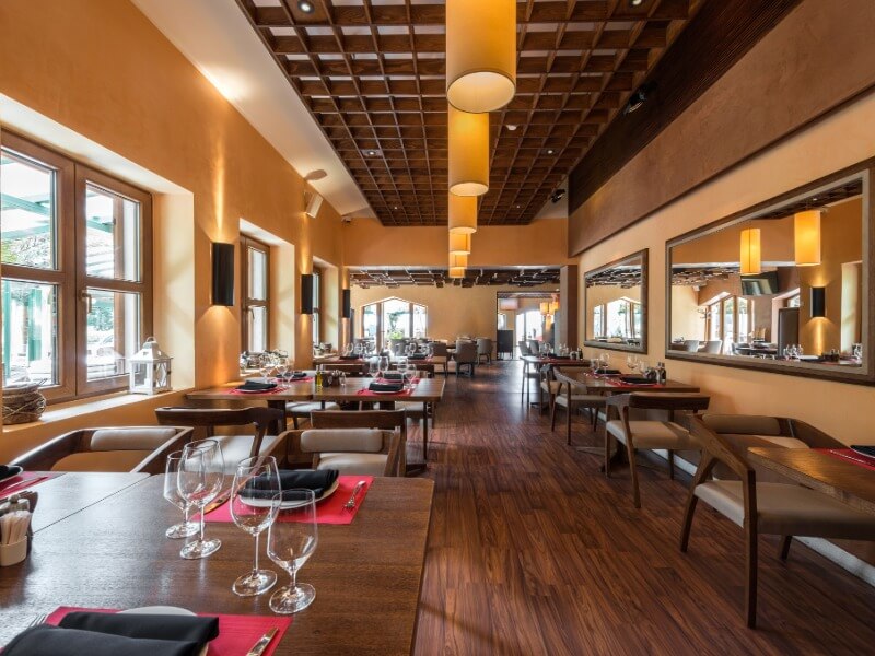 Restaurant dining room with warm lighting, wood ceiling, and table settings