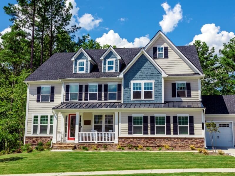 Two-story home exterior with tan and blue-gray siding, stone base, and red front door