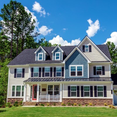 Two-story home exterior with tan and blue-gray siding, stone base, and red front door