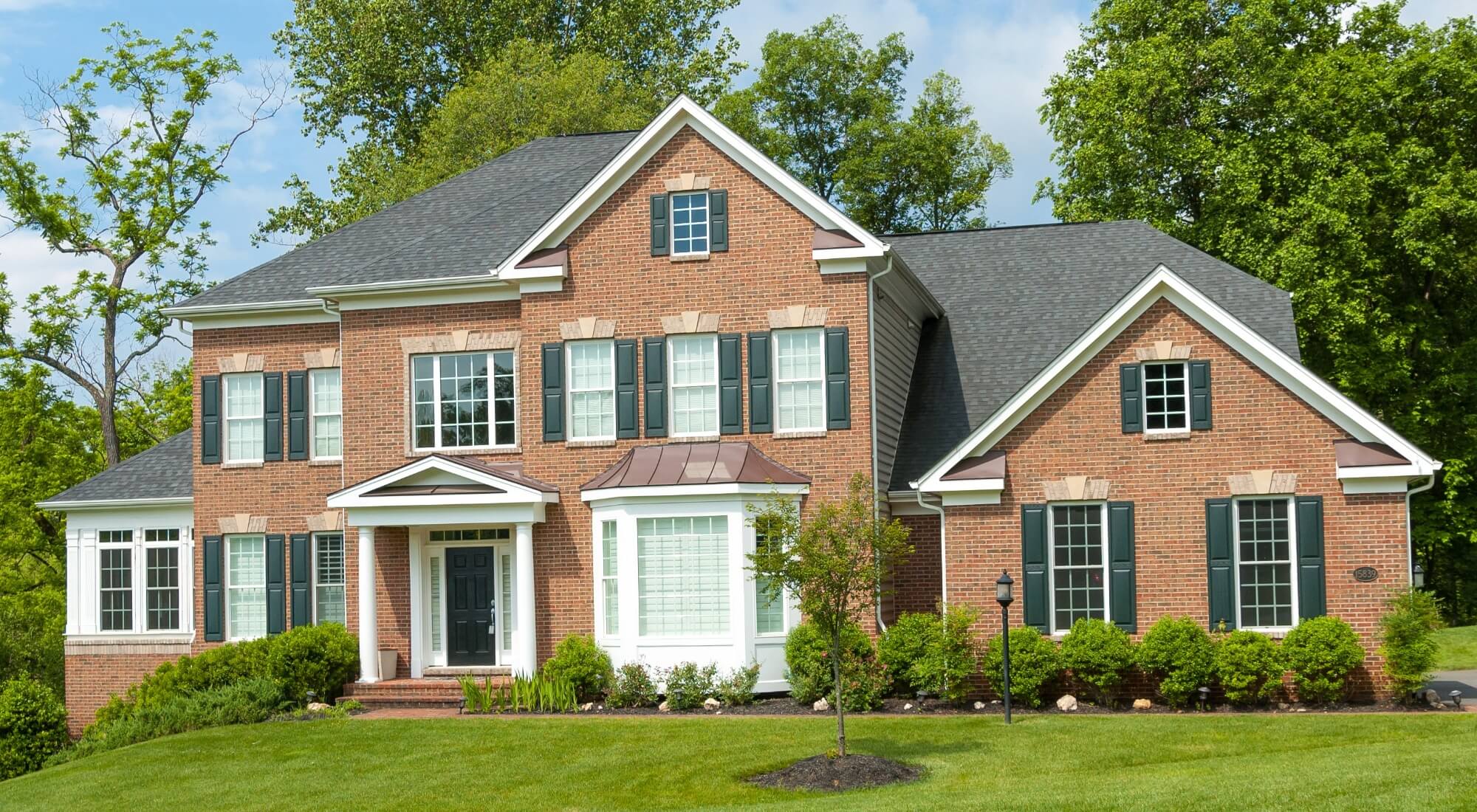 Two-story brick home with dark green shutters and white trim on a manicured lawn