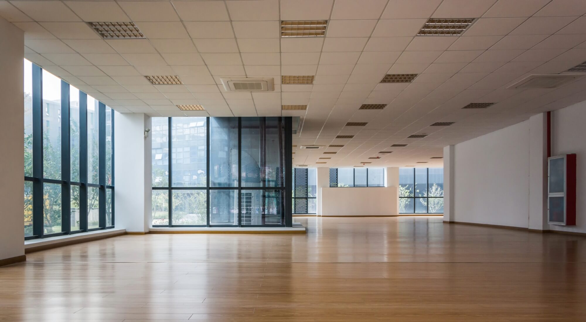 Empty commercial office space with wood floors, floor-to-ceiling windows, and white walls
