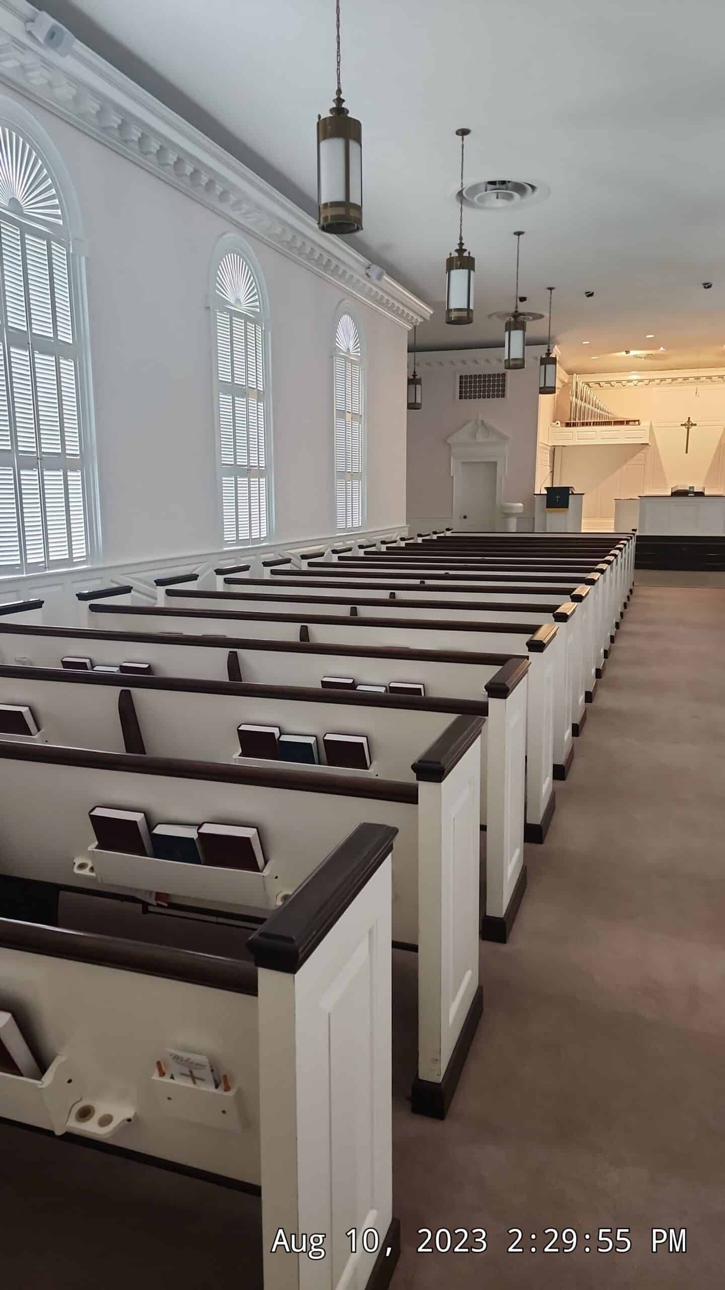 Church sanctuary with white pews, arched windows, and hanging pendant lights