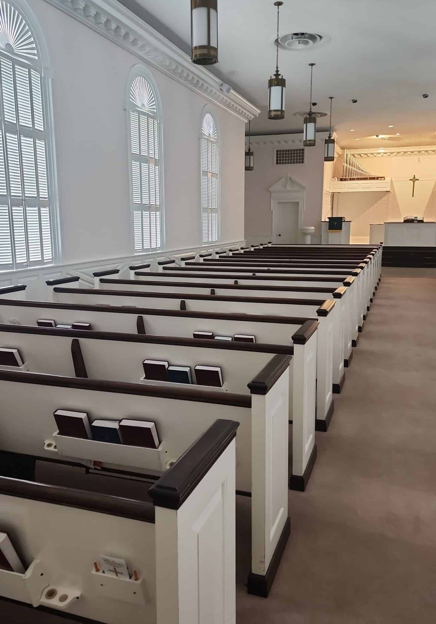 Church sanctuary with white pews, arched windows, and hanging pendant lights