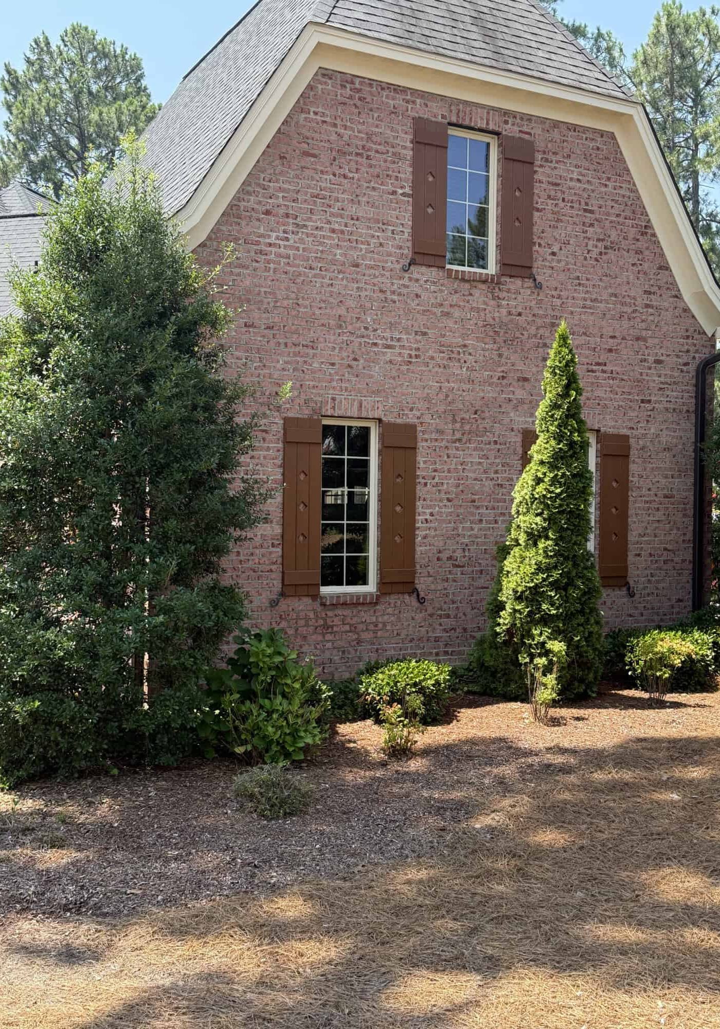 Brick gable-end home exterior with brown window shutters and landscaped foundation plantings